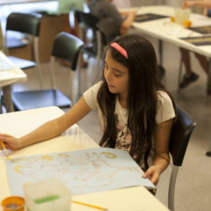 A child seated at a table writing on a poster.