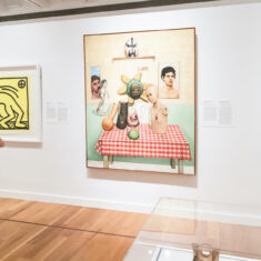 A woman stands in front of a row of paintings.
